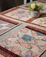 A close-up lifestyle shot of the Star-Patch placemats and runner on a dining table, featuring a blue floral star motif and a white floral centerpiece.
