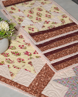 A perspective view showing the table runner and mats together, highlighting the contrast between the floral cream background and the rich brown scroll borders.