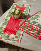 A side-angle view of the table setting, showing the red polka dot runner laid across the pine needle patterned mats.