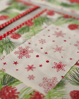 A close-up shot of the fabric, highlighting the detailed red snowflake prints against a white background and the green pine needle borders.