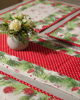 A focused view of the stacked placemats and runner, emphasizing the contrast between the bold red dots and the delicate green and white winter patterns.