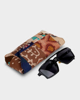 The eyewear case shown at an angle alongside a pair of dark sunglasses, illustrating its practical 7" length and structured, travel-ready form.