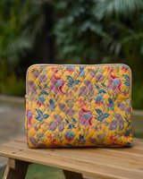 A front-facing view of the bag standing upright on a wooden bench, showcasing the dense teal vine and pink floral pattern against a lush, natural green background.