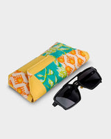 The eyewear case shown at a tilted angle alongside a pair of dark sunglasses, demonstrating its practical 7" length and structured, protective form.