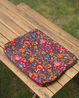 A high-angle perspective of the bag lying flat on a wooden slatted table, showcasing the full botanical pattern and the structured 2" depth of the quilted textile.