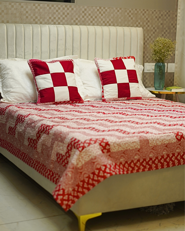 A cozy bedroom setup featuring the Red & White Chevron Quilted Bed Set on a bed with a white fluted headboard, styled with two bold checkerboard-patterned shams.