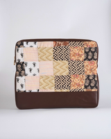 A handcrafted quilted laptop bag featuring a striking patchwork of earthy neutrals, including deep browns, warm ochres, and cream. The design showcases bold chevron waves and delicate paisley block prints above a rich, dark brown base.