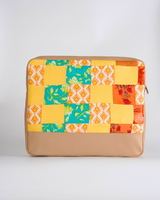 A handcrafted quilted laptop bag featuring a high-energy patchwork design in marigold yellow, turquoise, and burnt orange. The textile patterns include traditional block-printed florals and geometric diamond motifs, set above a clean, tan-colored base.