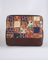 A handcrafted quilted laptop bag featuring a mosaic of deep cocoa browns, indigo blues, and cream floral patchwork. The design includes stylized leaf motifs and block prints above a smooth, dark chocolate-brown base.