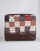 A handcrafted quilted laptop bag featuring a sophisticated patchwork of cream, terracotta red, and deep indigo. The design includes traditional floral block prints and striped textile patterns, finished with a smooth, dark chocolate-brown base.