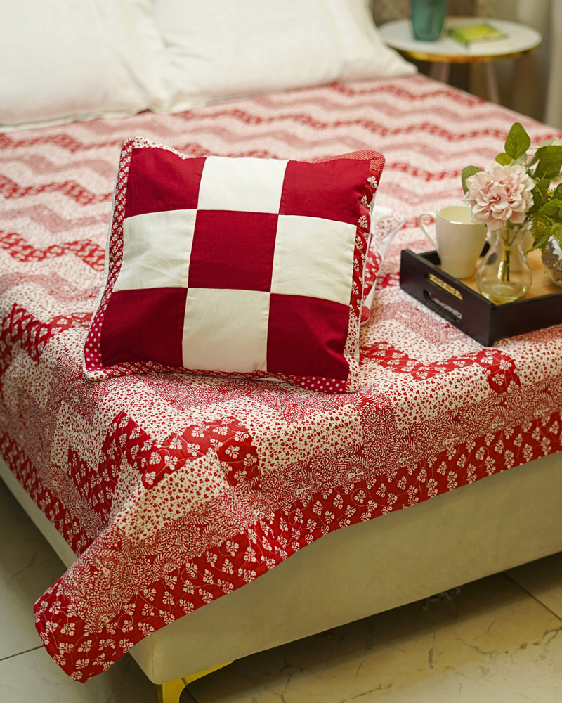 A focused view of one checkerboard sham resting on the quilt, emphasizing the contrast between the bold square patches and the delicate zig-zag strips.