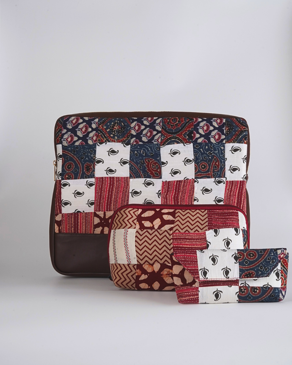 A coordinated three-piece set titled "Heritage Block Floral Essentials Trio," including a laptop bag, utility pouch, and eyewear case, all featuring a matching red, indigo, and ivory quilted patchwork with a dark brown base.