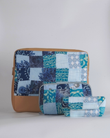 A coordinated set of three indigo and azure batik quilted accessories: a large laptop bag, a medium utility pouch, and a small eyewear case, all featuring a blue patchwork design with a tan base.
