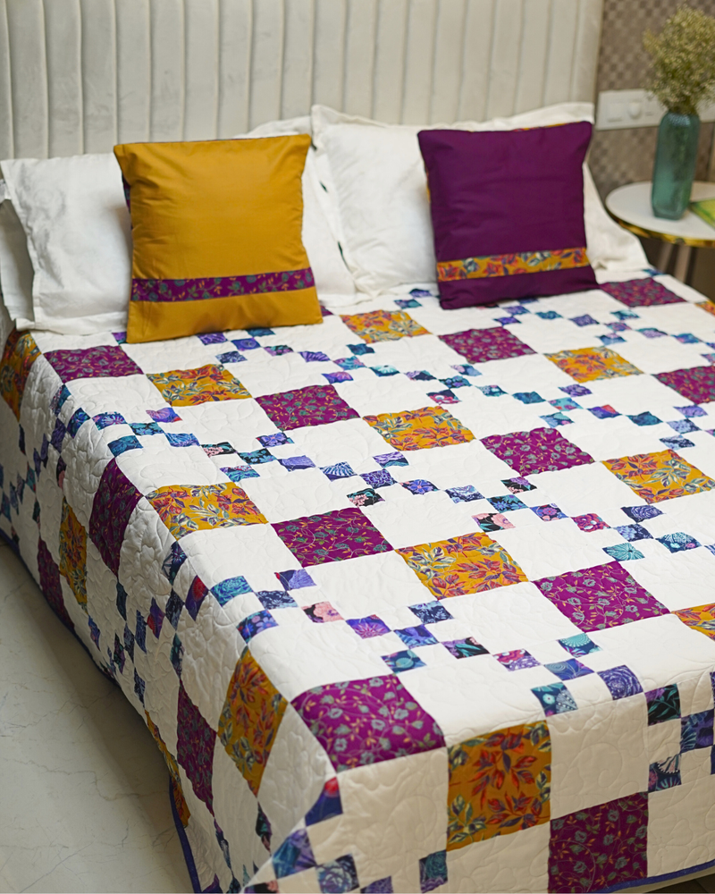 A wide view of the bed from the front, showcasing the full 74" x 74" quilt and two decorative shams in mustard yellow and deep purple.