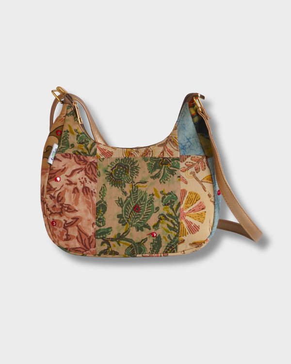 A studio shot of the Earthy Tones Patchwork Crescent Shoulder Bag, featuring a sophisticated curved silhouette and a patchwork of beige, olive green, and brown floral patterns.