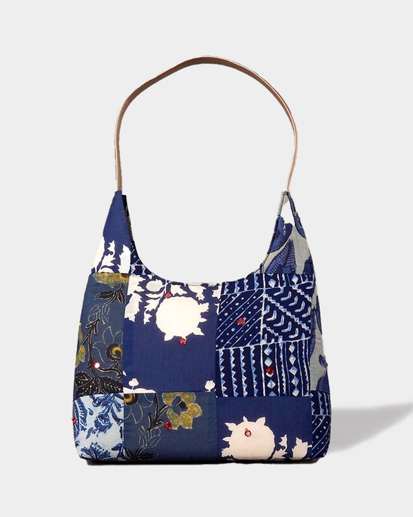 A studio shot of the Blue Floral Patchwork Hobo Bag, showcasing its relaxed silhouette and various indigo, navy, and cream floral and abstract patterns.