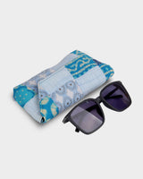 The eyewear case shown at an angle next to a pair of dark sunglasses, demonstrating its practical 7" length and protective, firm construction.