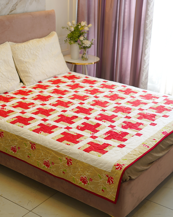 A cozy bedroom setup featuring the Crimson Lattice Cotton Bedquilt on a bed, styled with cream-colored pillows and a floral arrangement on a bedside table.