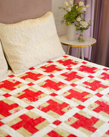 A side-angle view of the bed, showcasing the repeating red lattice pattern and the soft beige background of the quilt.