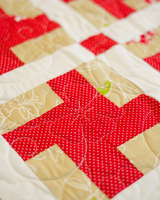 A close-up detail shot of the quilt's surface, focusing on the fine quilting stitches and the contrast between the red polka-dot lattice and the cream fabric.