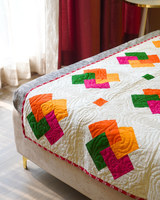 An angled view of the quilt draping over the side of the bed, showcasing the floral border and the clean, handcrafted finish of the textile.