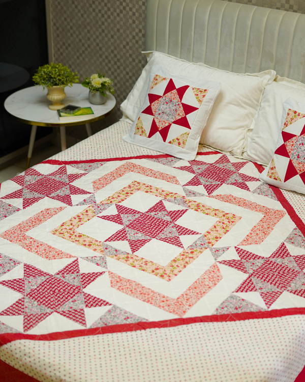 A high-angle shot of a bed styled with the Red & White Star Quilt and matching decorative shams, highlighting the central star patchwork design and the clean white polka-dot base.