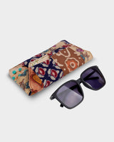 The Woven Floral Eyewear Case shown at an angle alongside a pair of sunglasses, illustrating its practical 7" length and sophisticated, portable design.
