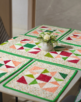 A beautifully arranged dining table showcasing the Pinwheel & Micro-Floral runner and placemats, topped with a white floral centerpiece to highlight the fresh, green aesthetic.