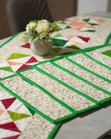 A side-angle view of the table setting, showing the repetitive green borders of the stacked placemats and the runner extending down the table.