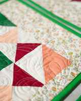 A macro shot of the pinwheel design, emphasizing the handcrafted textile details and the blend of peach, red, and green fabrics.